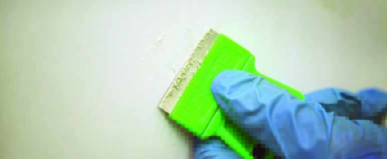 Hand of a cleaner wearing a glove cleaning bathroom tiles with a scraper